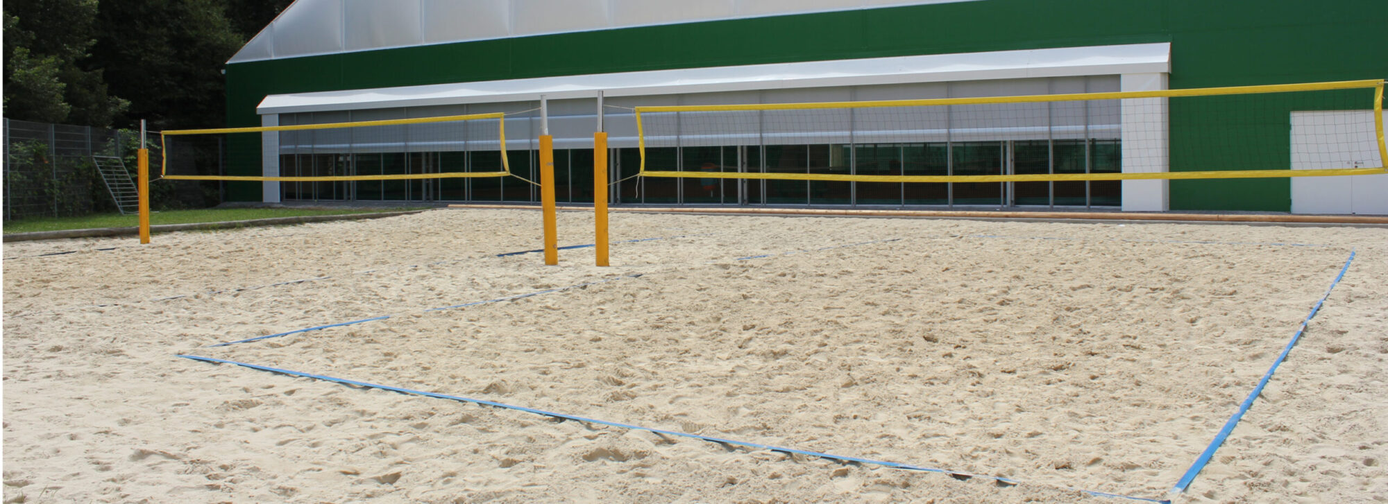 Ein Beachvolleyballplatz auf der Marswiese mit feinem Sand, umgeben von Natur und blauen Himmel im Hintergrund.